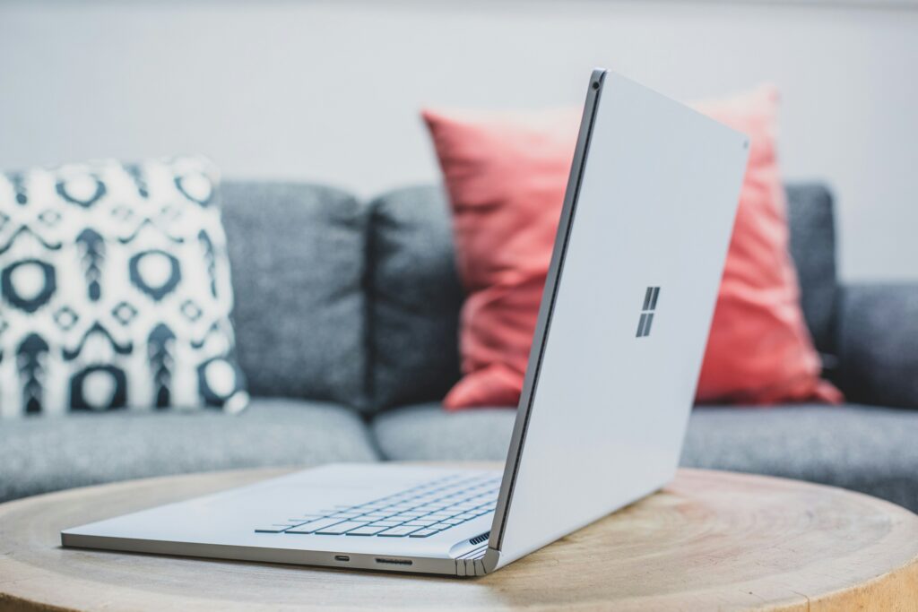Zilvergrijze Microsoft Surface-laptop opengeklapt op een houten salontafel, met op de achtergrond een grijze bank en decoratieve kussens.