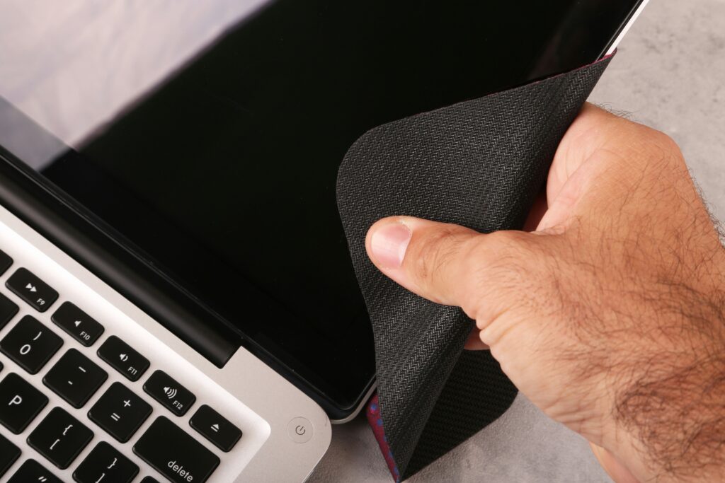 Persoon die voorzichtig een Microsoft Surface laptop schoonmaakt met een microvezeldoekje op een bureau.