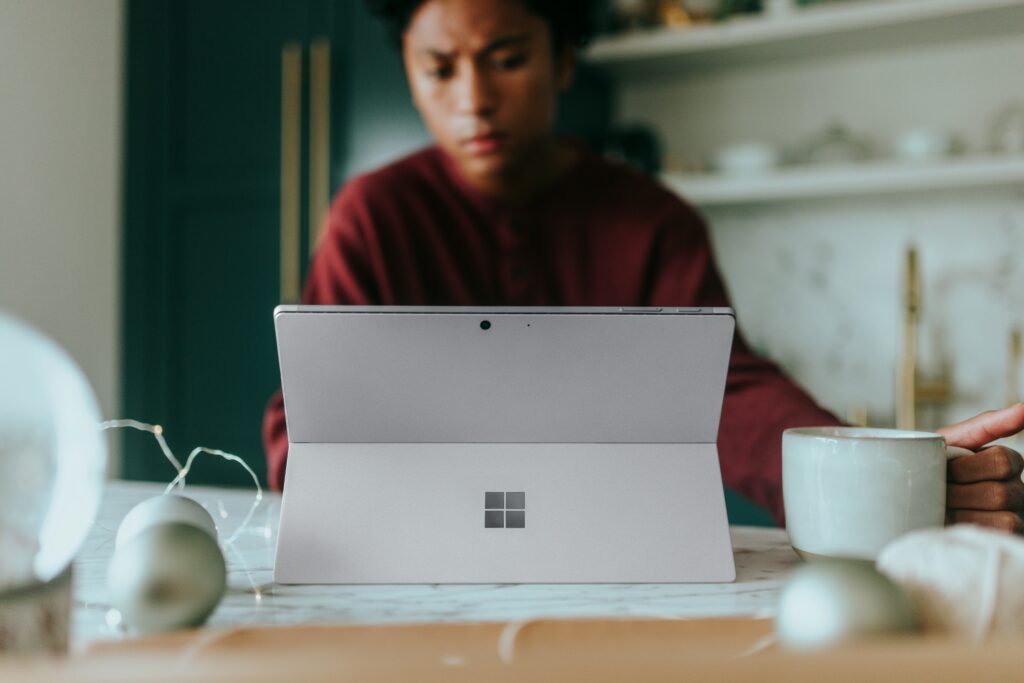 Vrouw werkt geconcentreerd op haar Microsoft laptop terwijl ze een kopje koffie vasthoudt, zittend aan een bureau in een lichte, moderne omgeving.